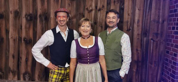 David Saam, Maria Bauer und Werner Aumüller in trachtenähnlicher Kleidung vor einer holzgetäfelten Wand