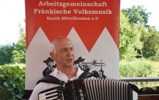 Mann mit Akkordeon vor PopUp der Arge Fränkische Volksmusik