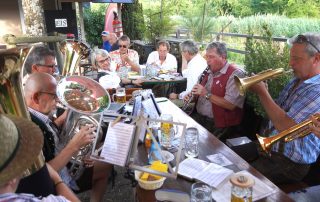 Musizierende und Publikum an Biergartentischen mit Geschirr und Noten