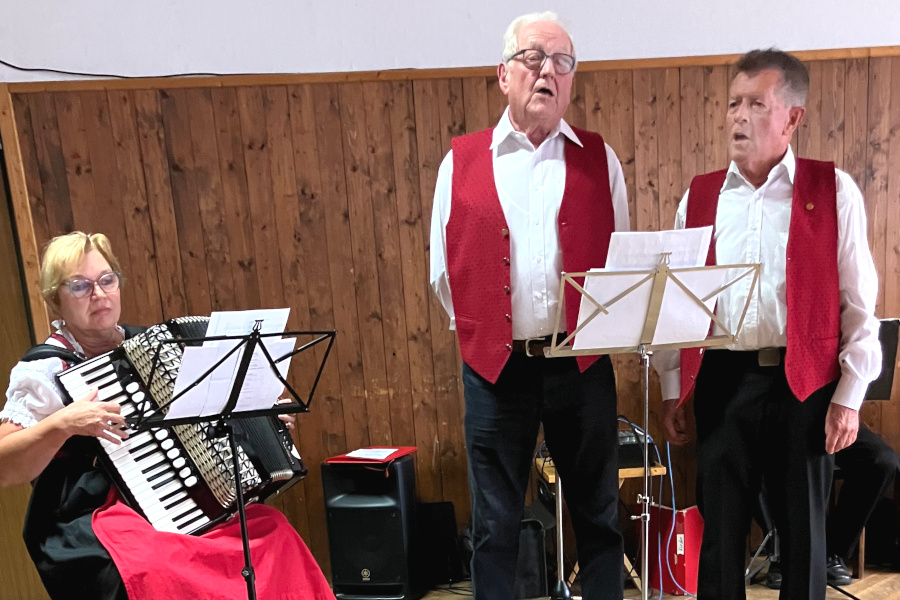 Acherwäldlers-Duo Eine sitzende Frau mit Akkordeon und zwei stehende singende Männer, davor jeweils ein Notenständer