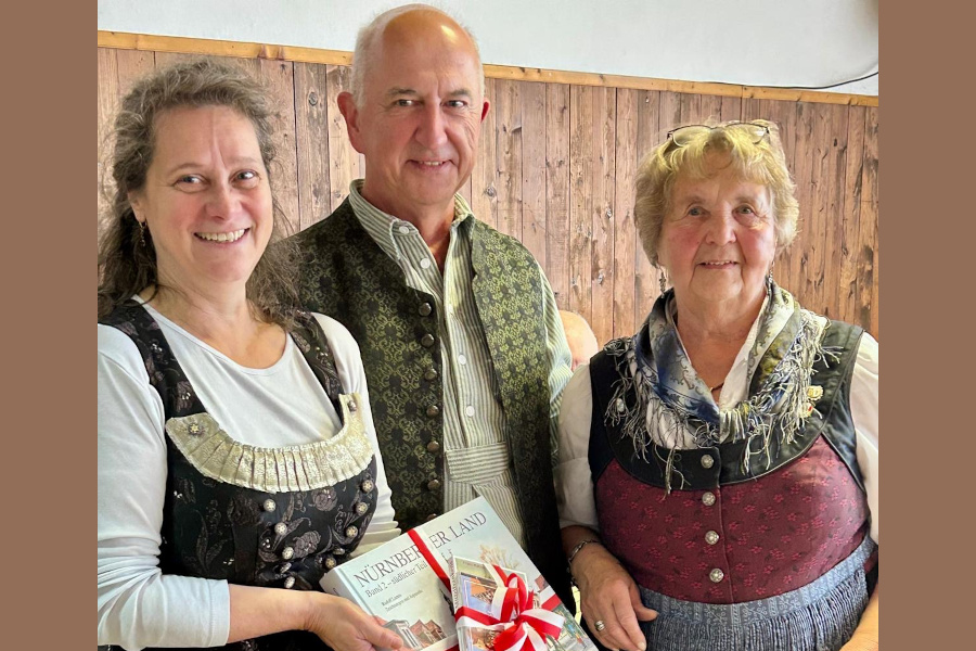 3 lächelnde Personen mit Geschenkbuch in der Hand